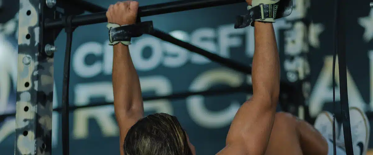 Mujer ejecutando dominadas en una barra fija dentro del gimnasio