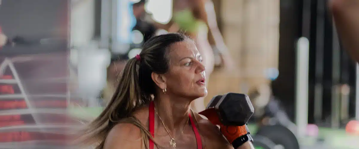 Mujer levantando una mancuerna mientras entrena fuerza de brazos en gimnasio