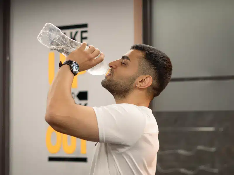 Deportista bebiendo agua durante un descanso entre ejercicios en el gimnasio