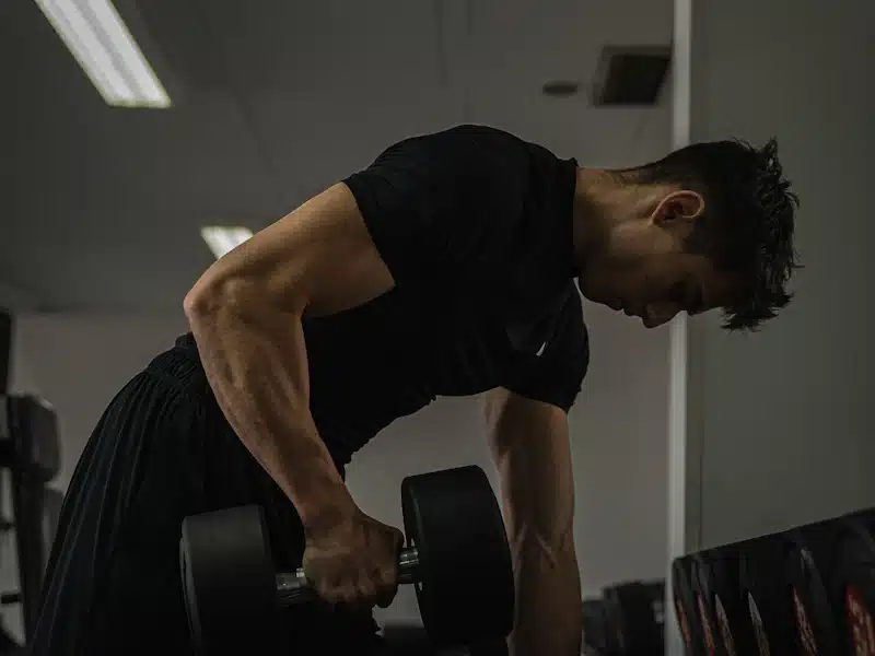 Deportista musculado realizando remo con mancuerna durante su sesión de gimnasio