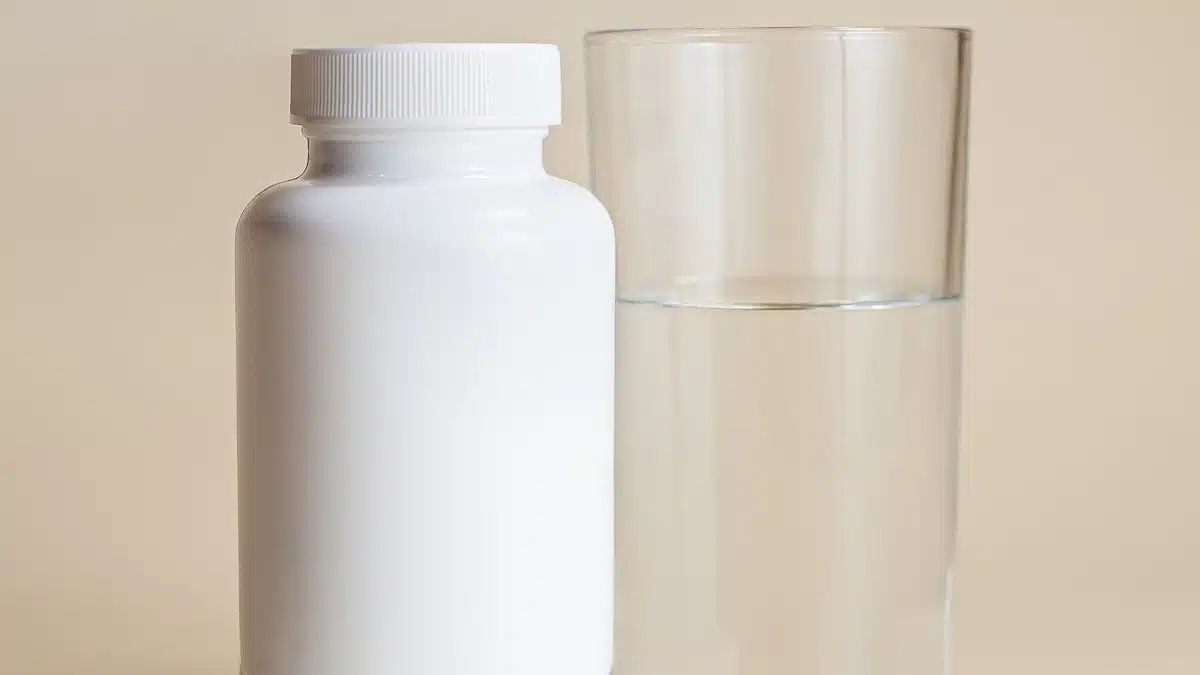 Dos recipientes de laboratorio con cápsulas de suplementos sobre fondo claro