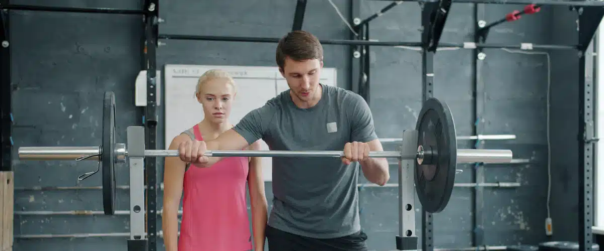 Entrenador supervisa a una mujer que levanta pesas en gimnasio