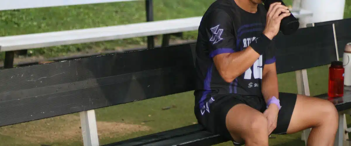 Futbolista sentado en el banquillo bebiendo agua durante un descanso