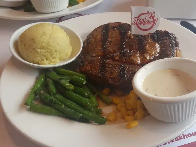 Plato con carne cocinada y verduras junto a una guarnición de patata