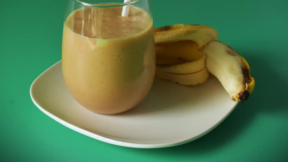 Vaso de batido de plátano con fruta fresca servido para desayunar